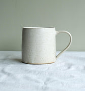White handmade ceramic mug on a linen surface with a plain background